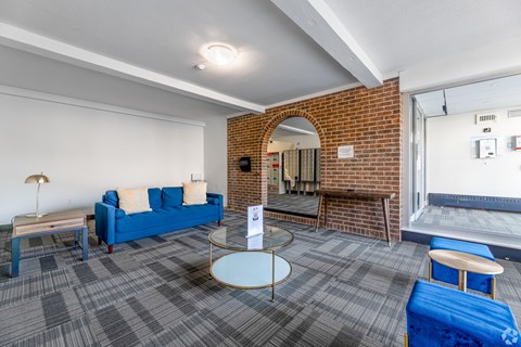A room with a blue couch, a round table, and a brick wall.