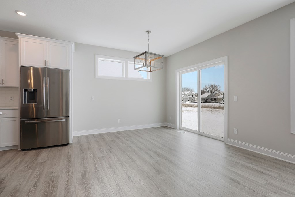 an empty living room with a stainless steel refrigerator and a door to a patio