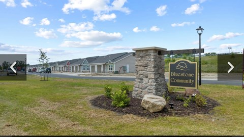 A sign for Bluestone Community stands in a grassy area in front of a row of houses.