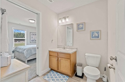 A bathroom with a white toilet, sink, and a bedroom with a window in the background.
