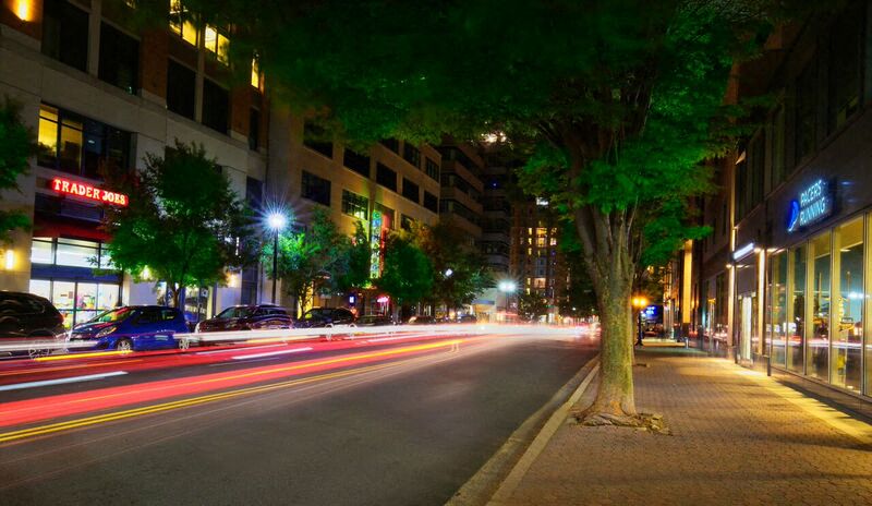 a city street at night with cars and a tree