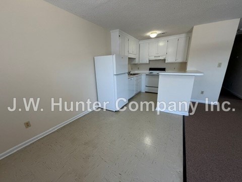 A kitchen with white cabinets and appliances in a room with a carpeted floor.