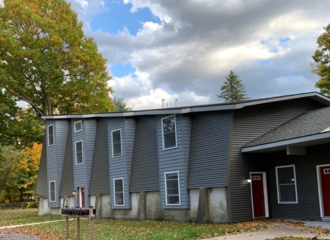 a gray house with a red door and a cloudy sky