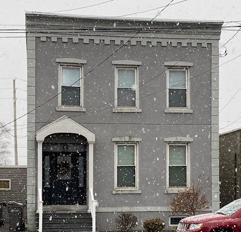 A grey building with a red car parked in front.