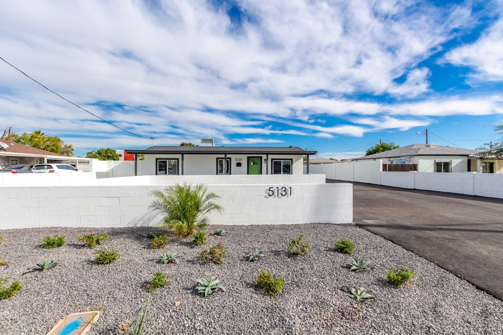 a home with a white wall and a driveway with plants in front of it