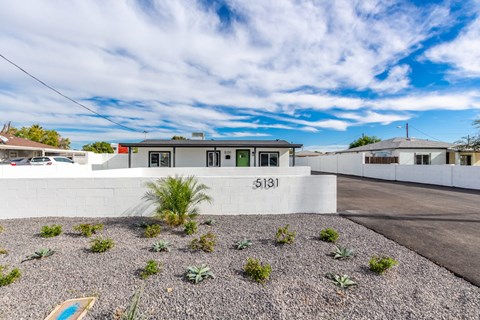 a home with a white wall and a driveway with plants in front of it
