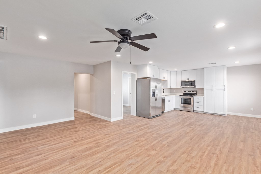 an empty living room with a ceiling fan and a kitchen