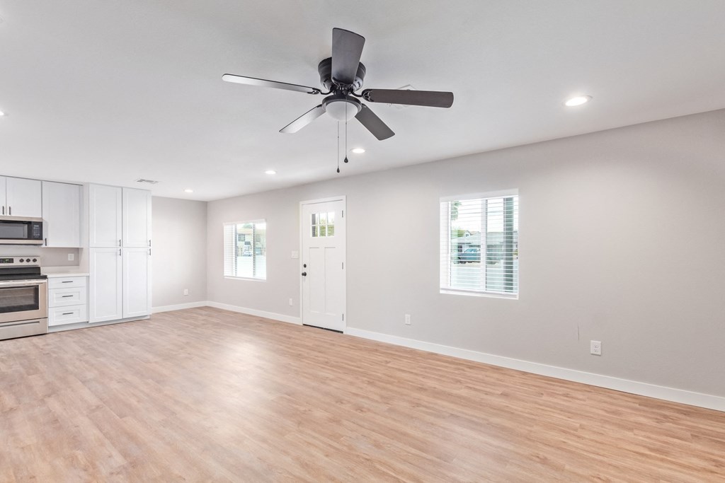 an empty living room with a ceiling fan and a kitchen