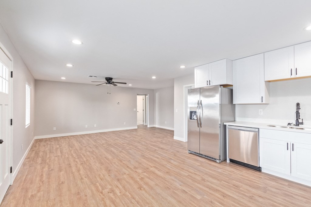 an empty living room with a kitchen and a ceiling fan