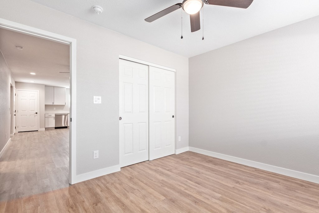 an empty living room with a ceiling fan and a door to a kitchen