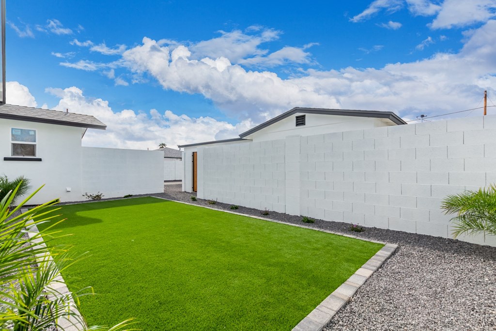 the backyard of a house with a green lawn and a white wall