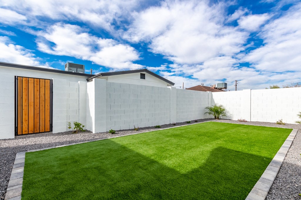 a backyard with a green lawn and a white fence
