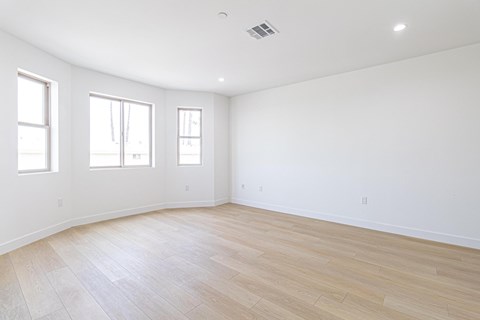 A large empty room with wooden floors and three windows.