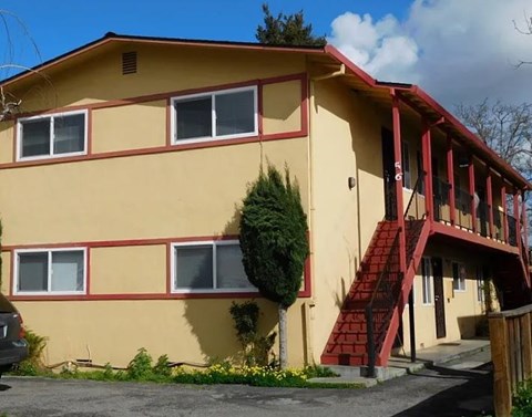 a yellow house with red stairs and a tree in front of it