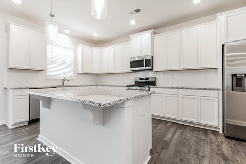 A kitchen with white cabinets and a marble island.