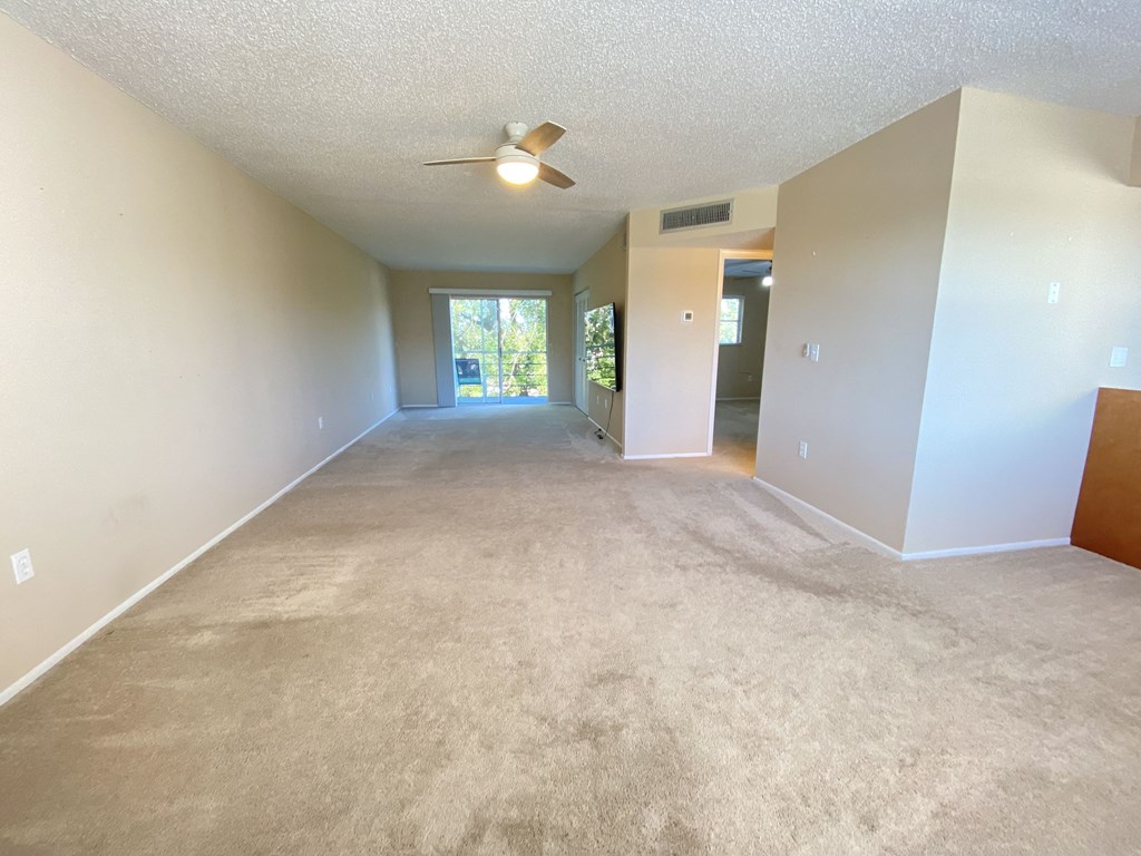 an empty living room with carpet and a ceiling fan