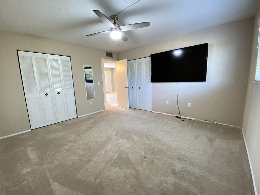 an empty living room with a ceiling fan and a tv