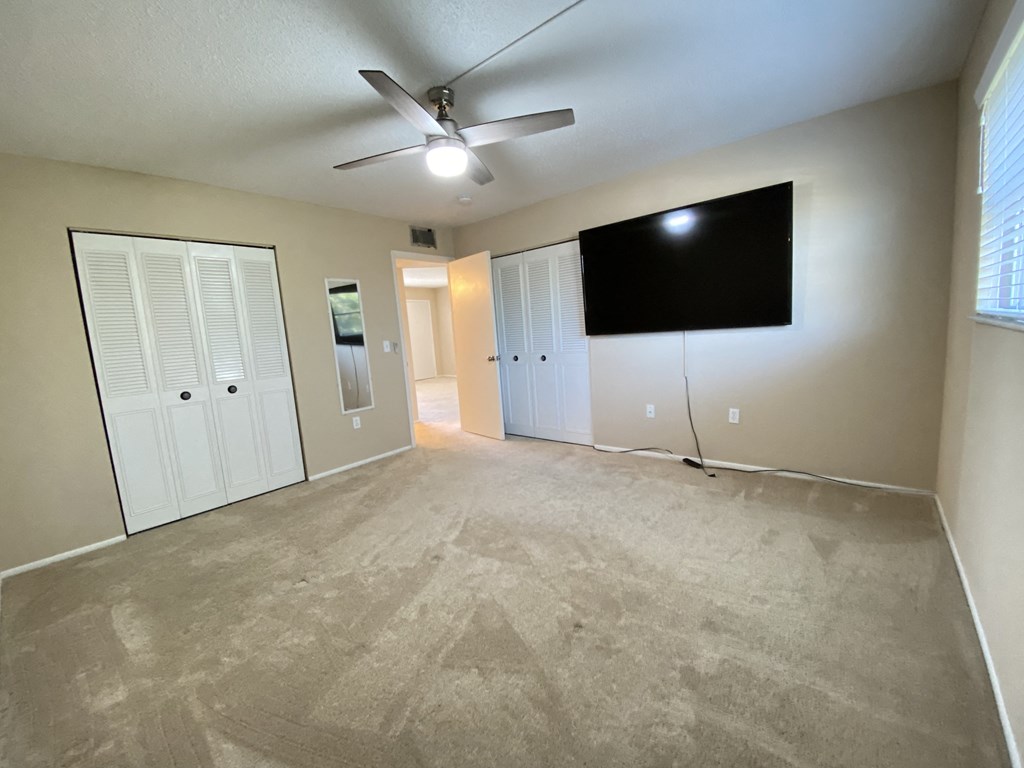 an empty living room with a ceiling fan and a tv