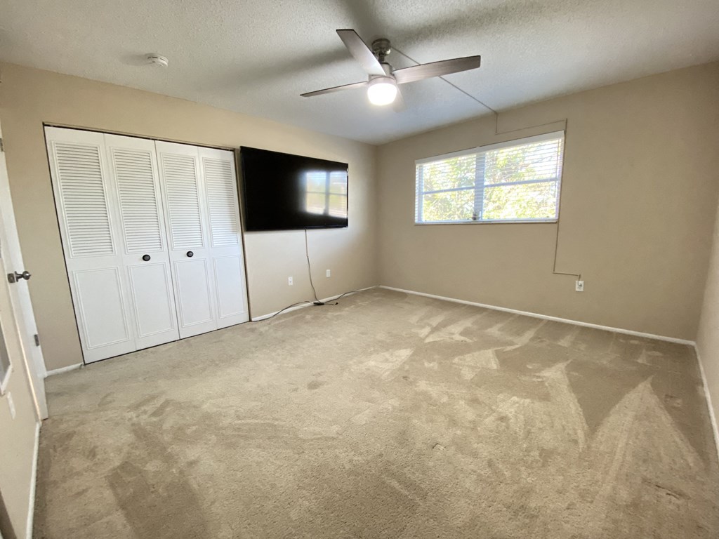 an empty living room with a ceiling fan and a tv