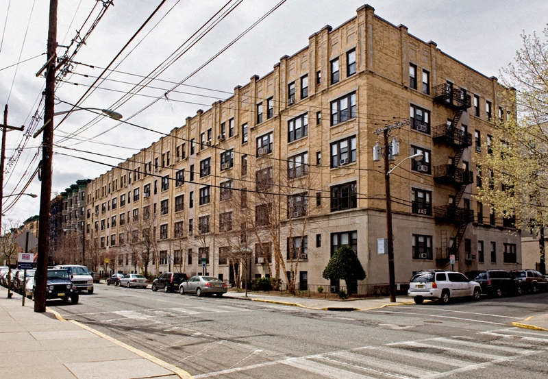 A street view of a residential building with cars parked on the side.