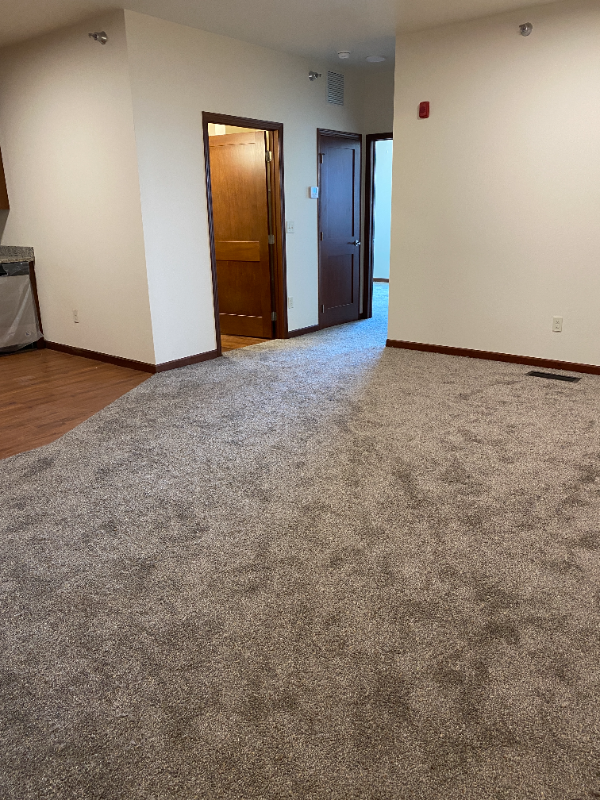 the living room and dining room of an empty house with carpeting and a door