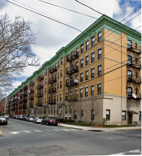 A row of brown and green buildings with cars parked on the street.