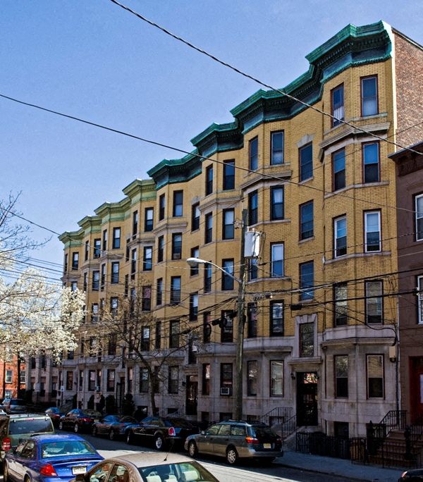 A row of brown and green buildings with cars parked in front.