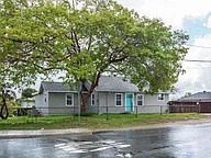 A house with a blue door is surrounded by a fence and a tree.