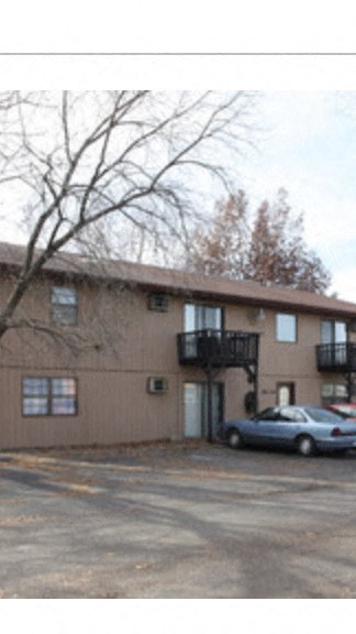 A car is parked in front of a brown building with a balcony.