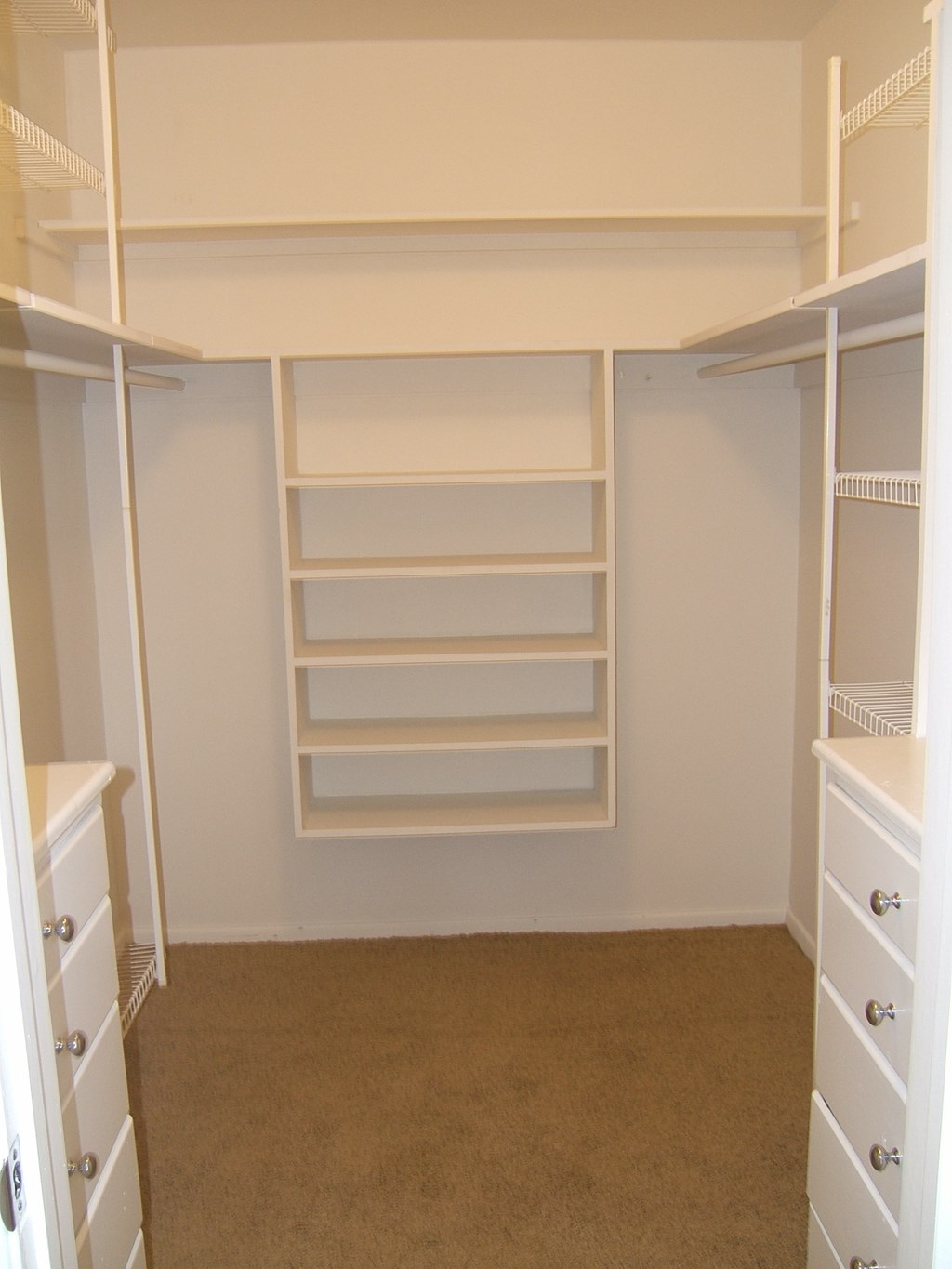 a walk in closet with white shelves and a carpet