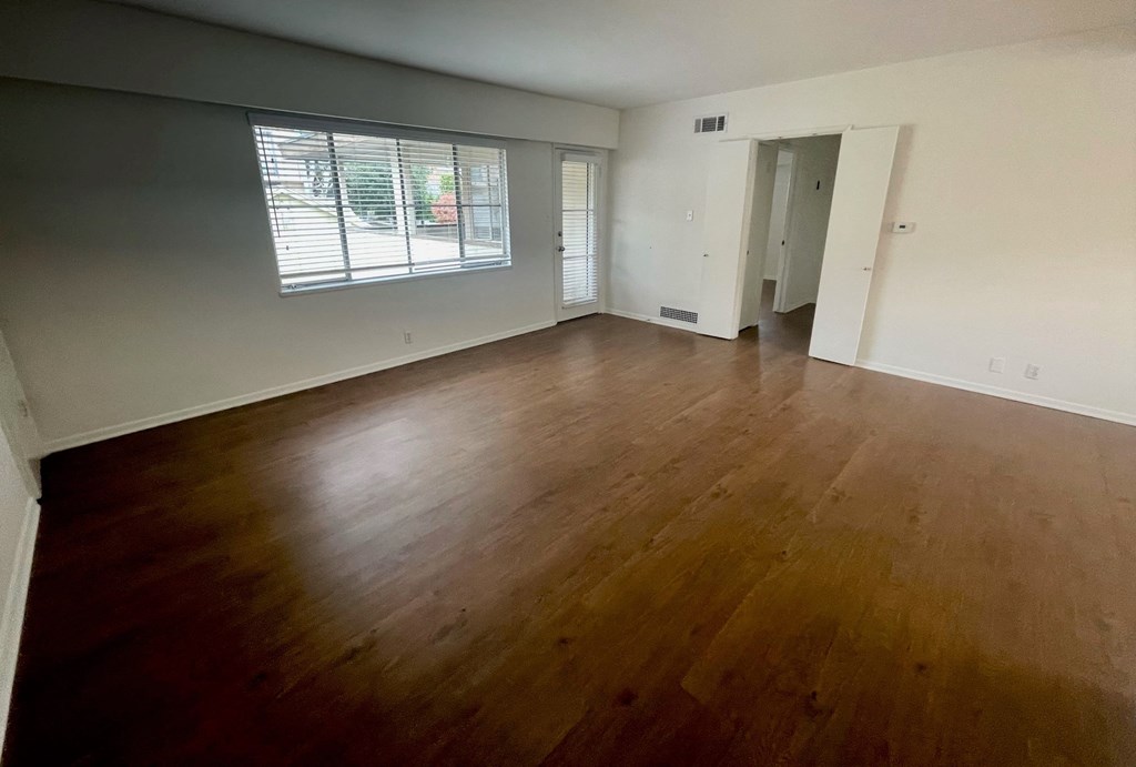 an empty living room with wood floors and a window