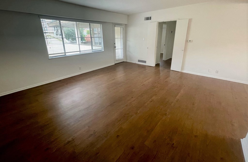 an empty living room with wood floors and a window