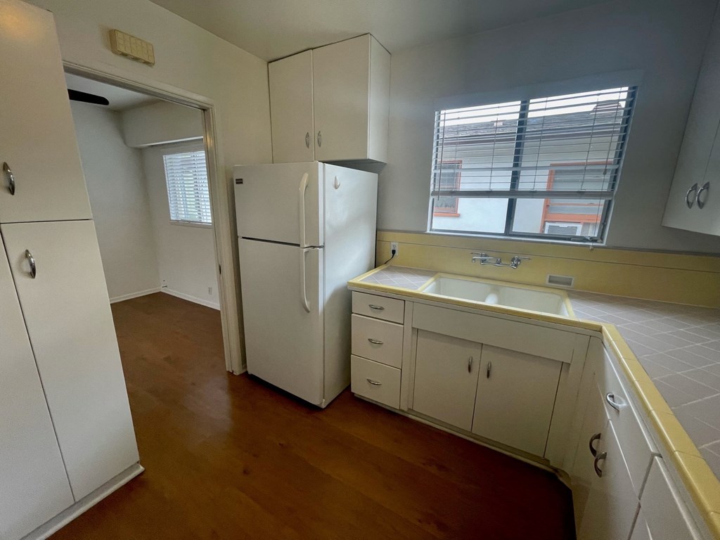 an empty kitchen with white cabinets and a refrigerator