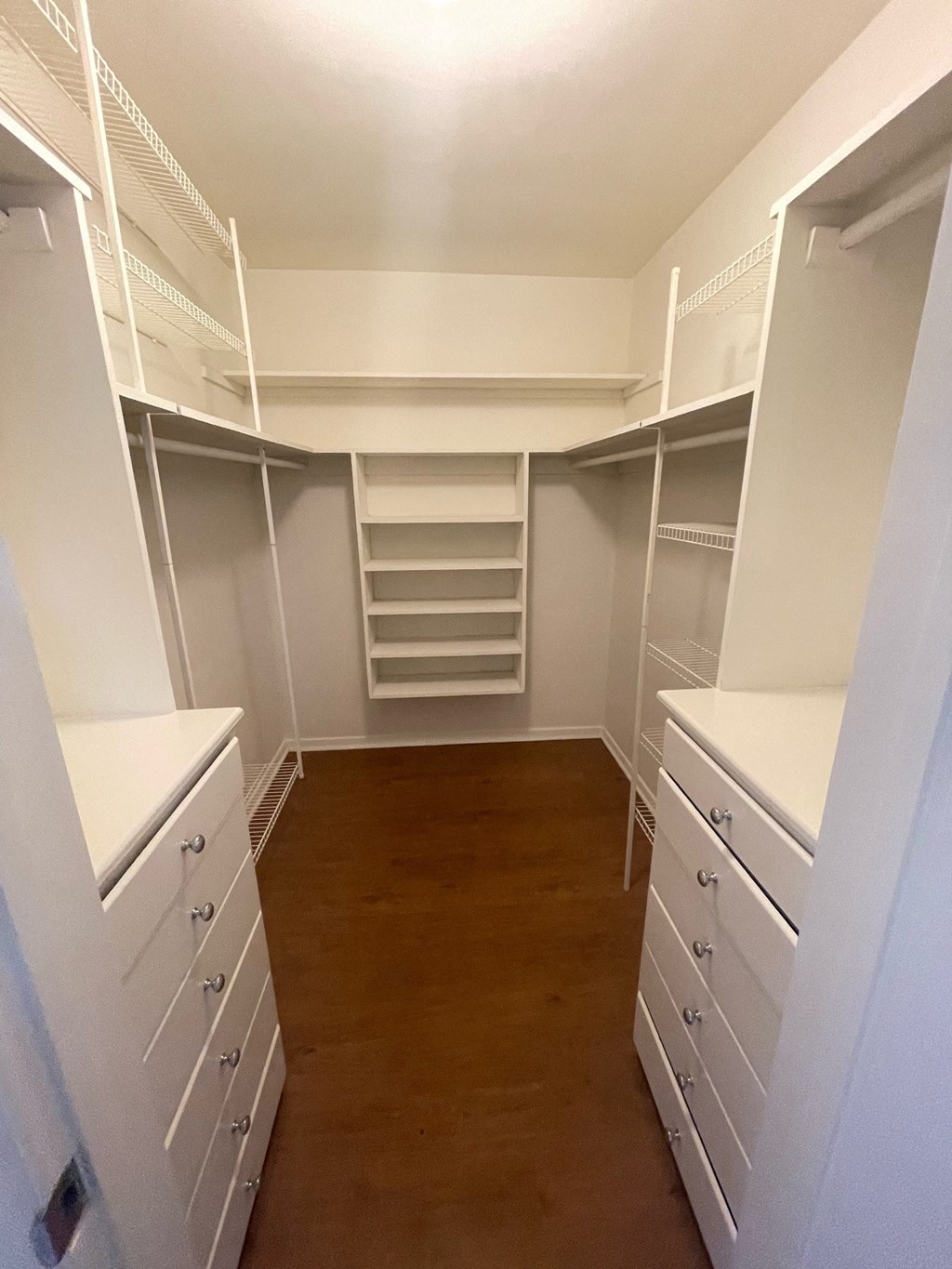 a walk in closet with white shelves and drawers
