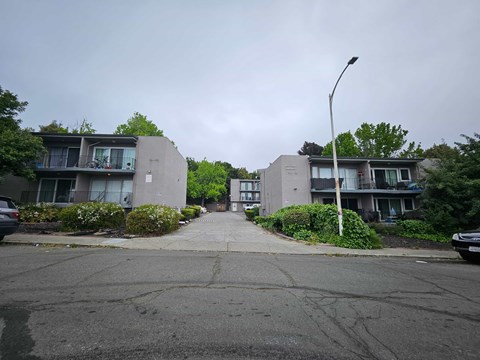 A street view of a residential area with two buildings on either side and a car parked on the right.
