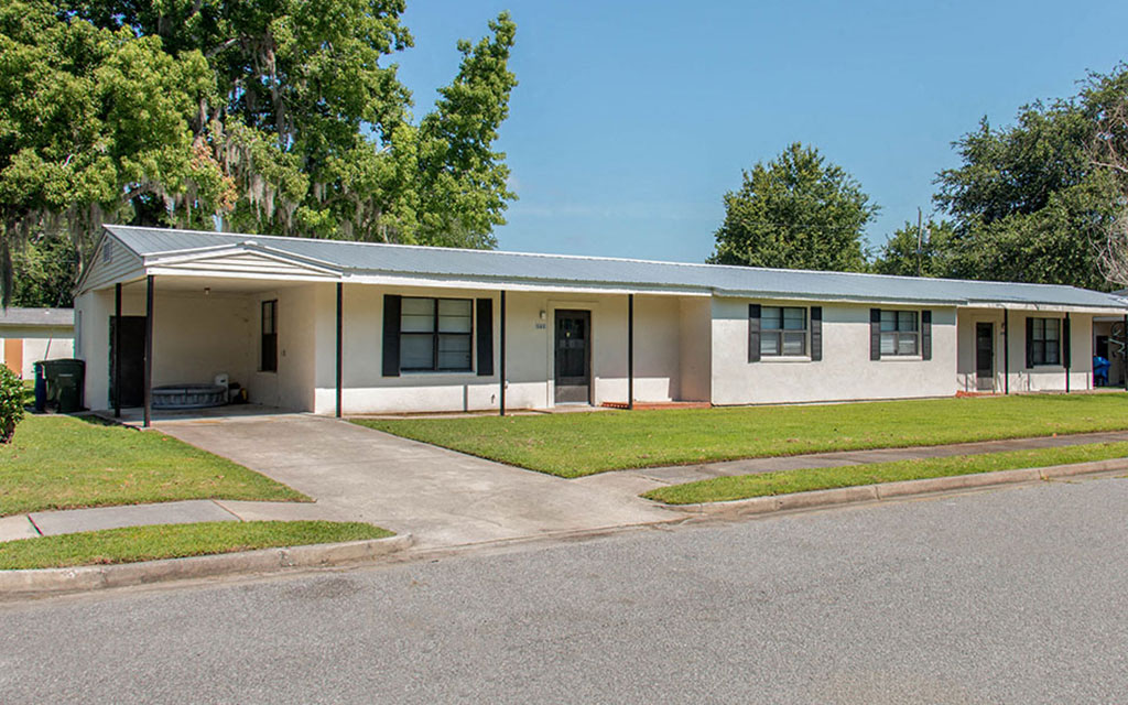 the front of a white house with a driveway and grass
