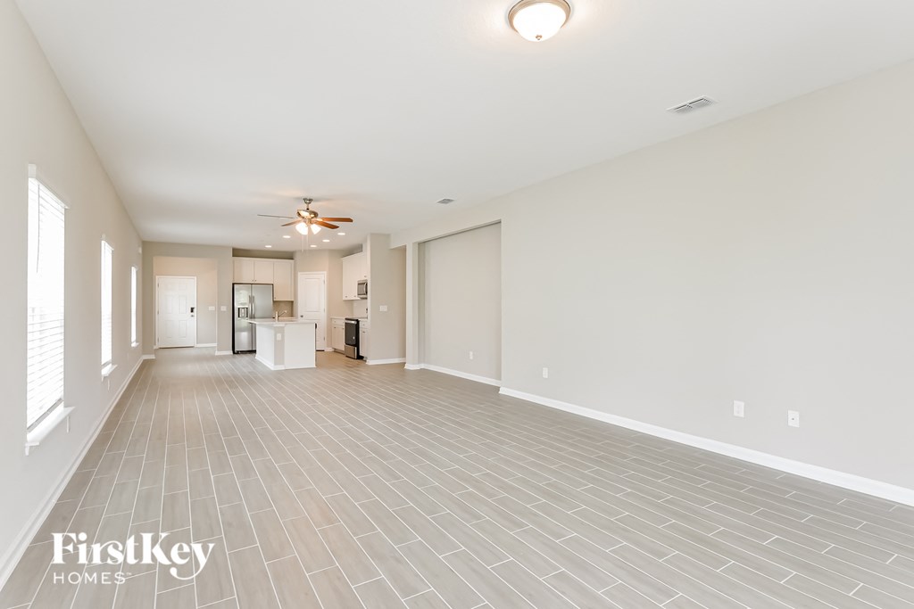 an empty living room with a ceiling fan and a kitchen