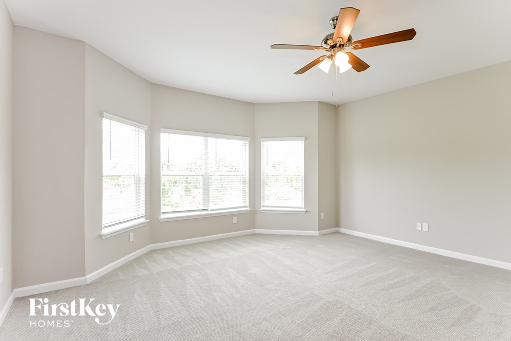 an empty living room with a ceiling fan and three windows