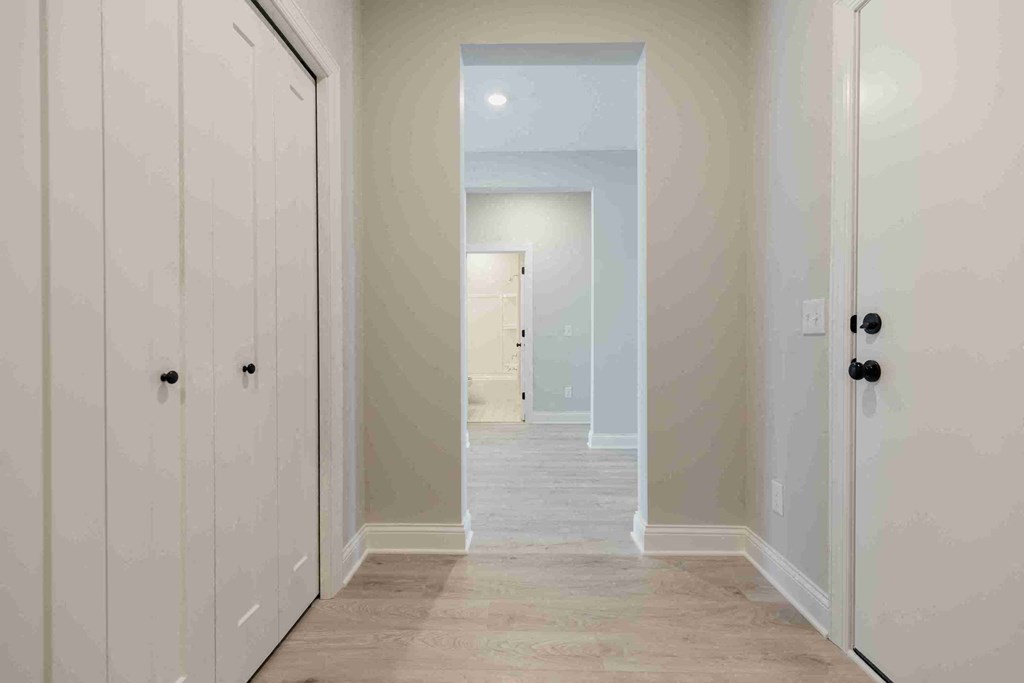 a long hallway with white cabinets and a door to a closet