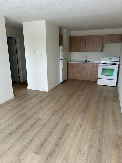 A kitchen with a white fridge and oven, and wooden flooring.