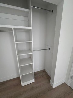 A white shelving unit with four shelves is in a corner of a room.