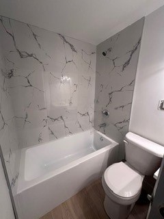A white toilet sits next to a bathtub in a bathroom with marble walls.