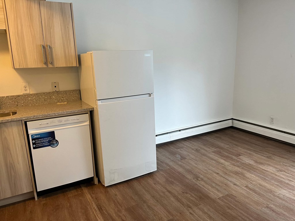A white refrigerator is in a kitchen with wood floors and cabinets.