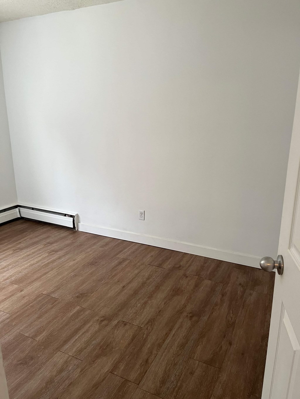A room with a white wall and a wooden floor.
