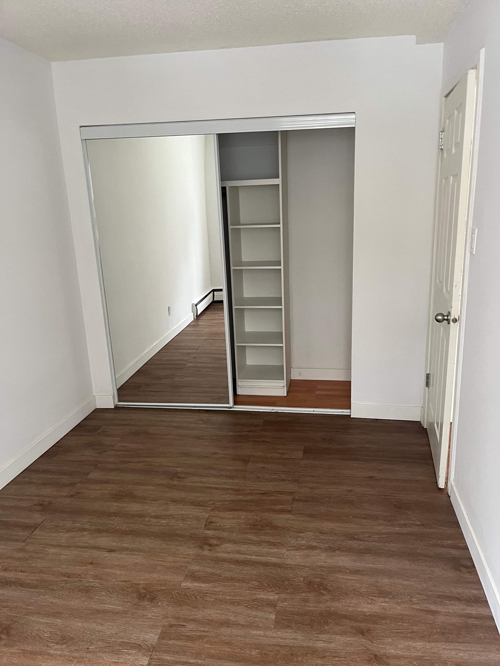 A room with a white door and a brown floor.