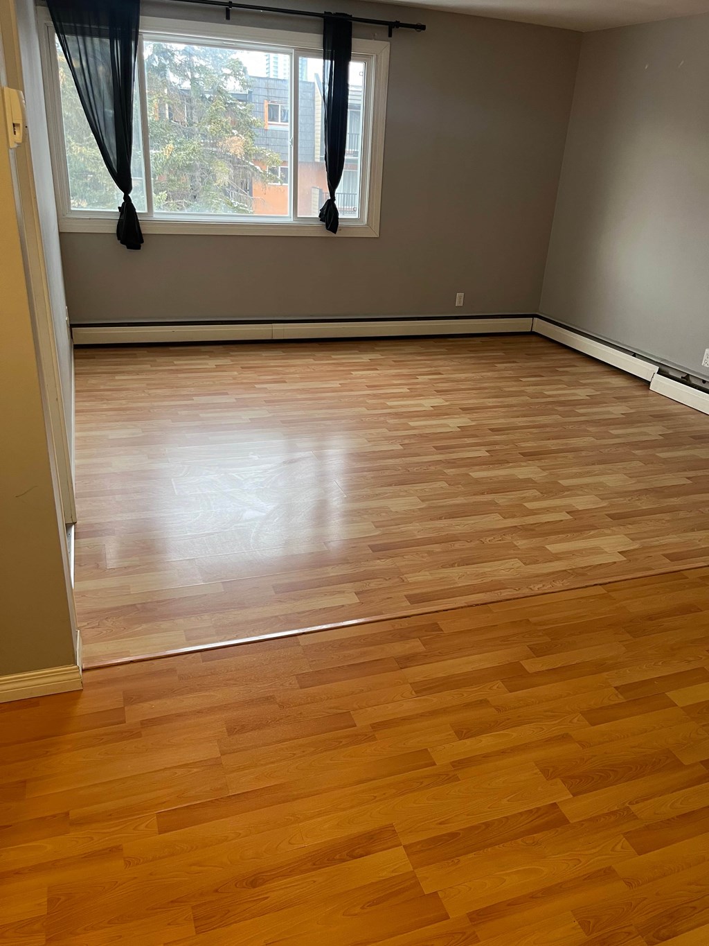 A room with wooden flooring and a window with black curtains.