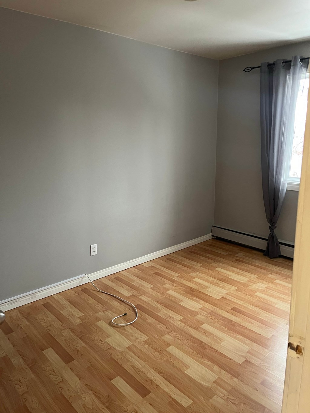 A room with wooden flooring and a window with curtains.