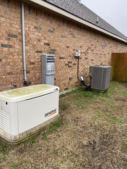 A white generator sits outside a brick building.