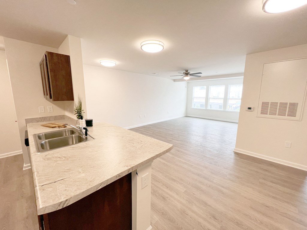an empty living room with a kitchen and a ceiling fan