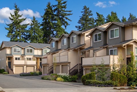 Row of two-story townhomes at Ballinger Place with attached garages, private entries, and tall evergreen trees.